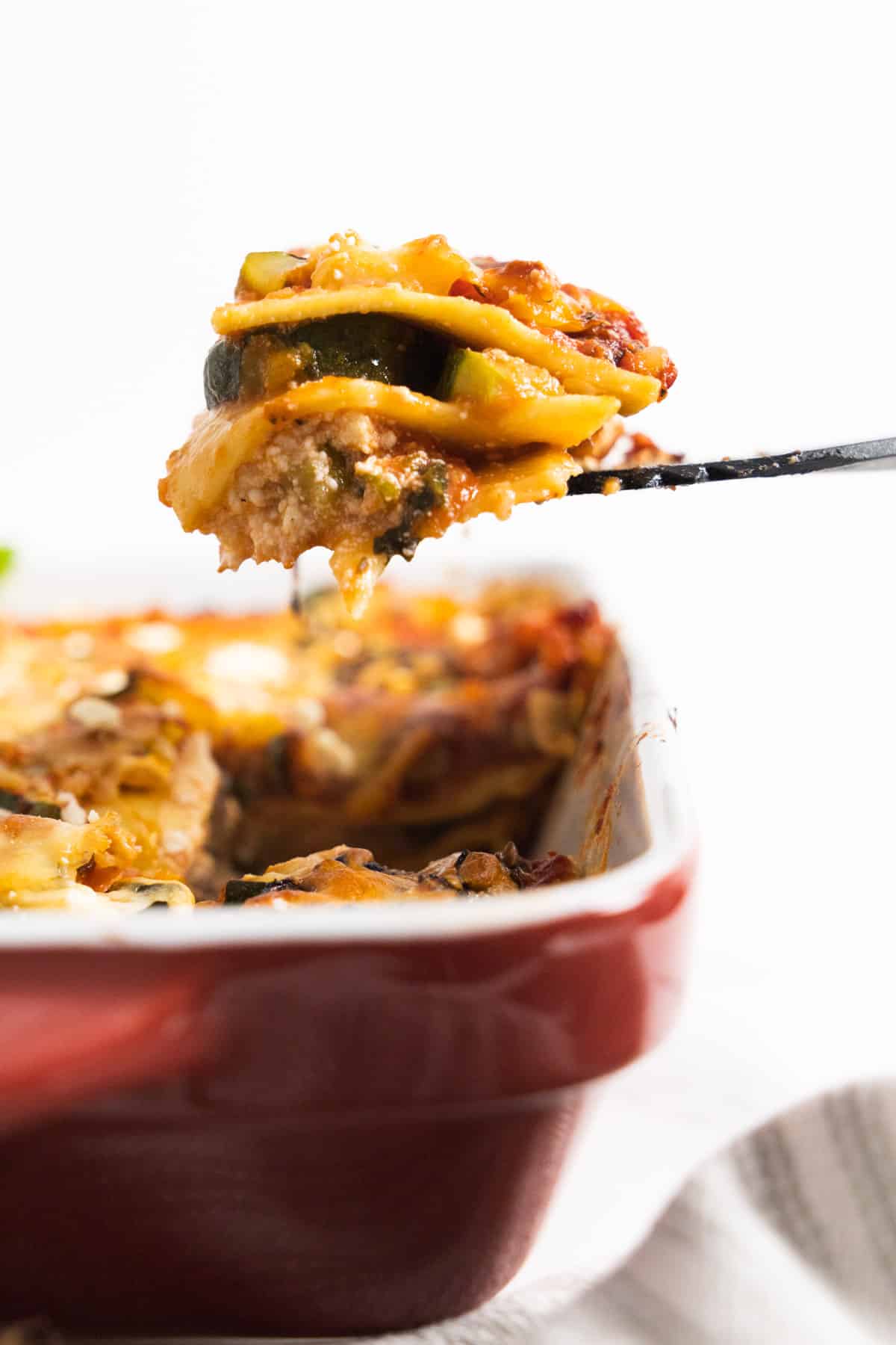 spatula holding a portion of lasagna over a red baking dish.