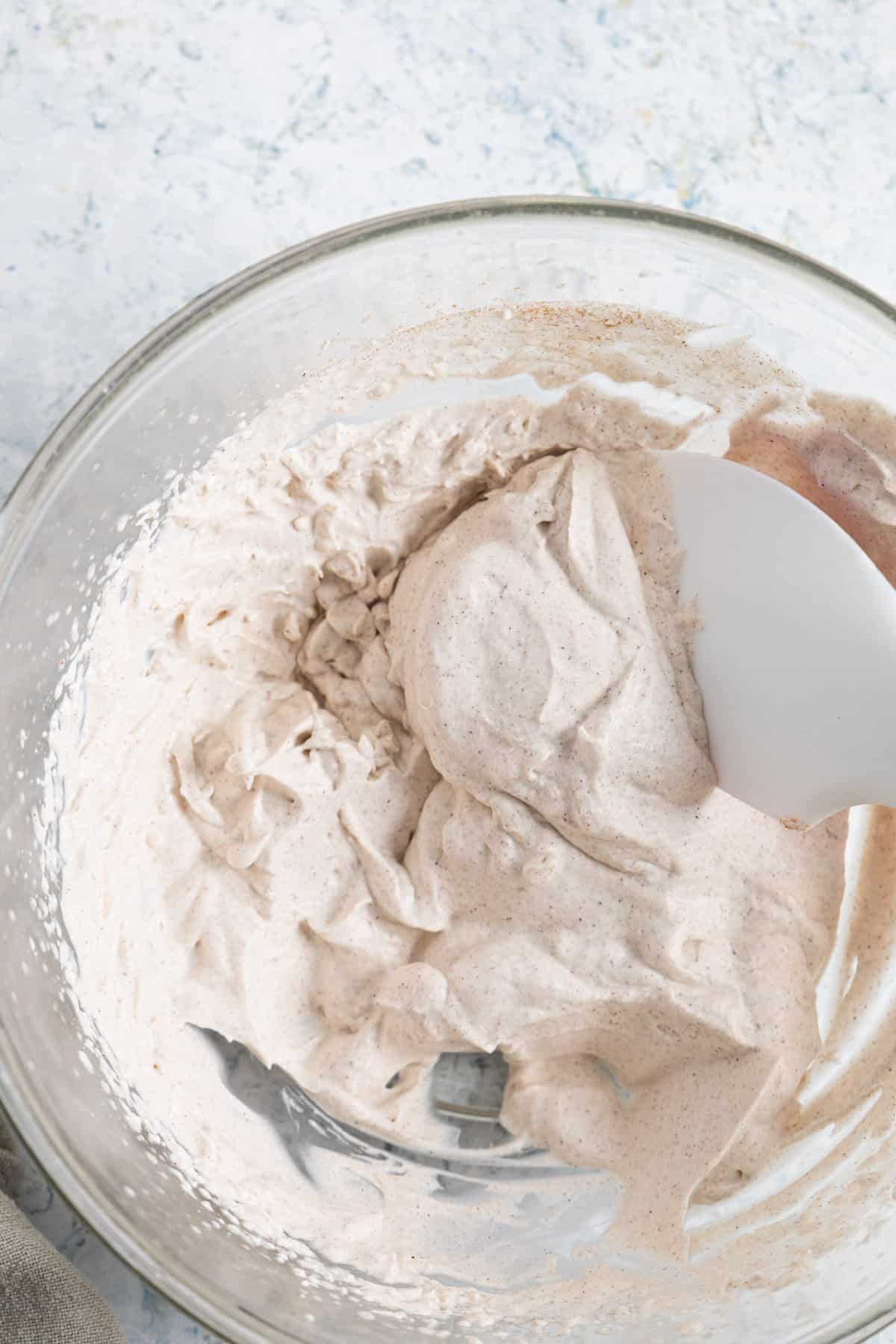 whipped cream in a transparent mixing bowl with a spatula.