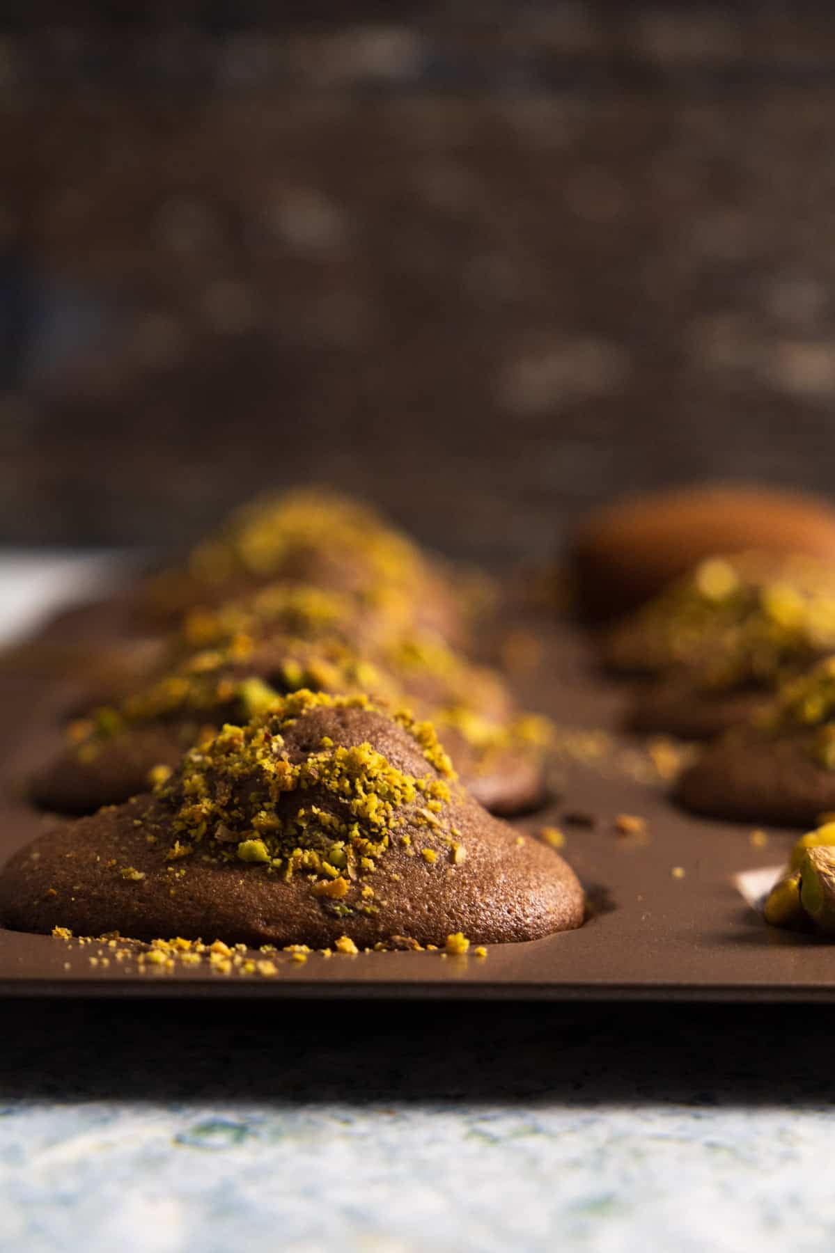 close up of a chocolate madeleines with pistachio in its mold. 