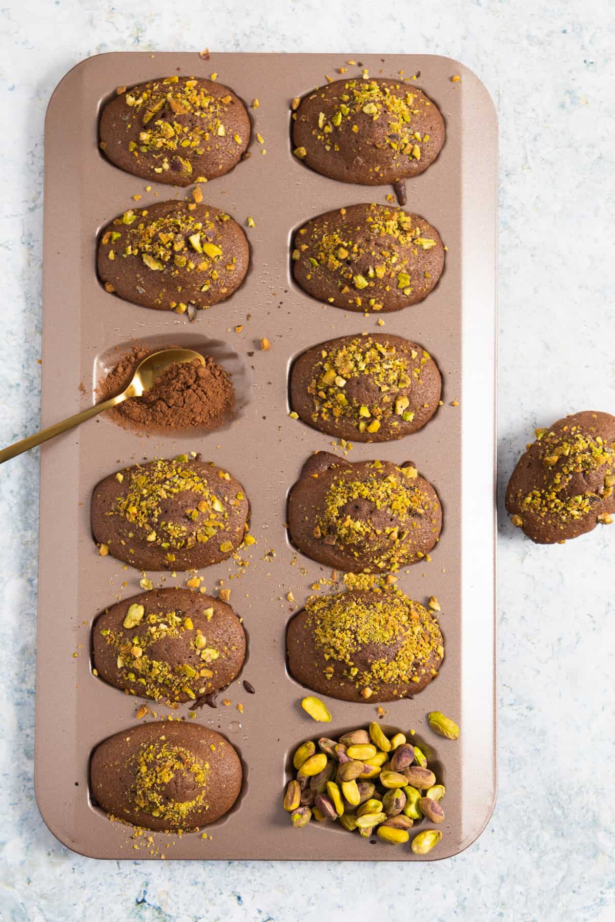 chocolate madeleines still in their mold and except one mold is filled with pistachio and one with cocoa powder.