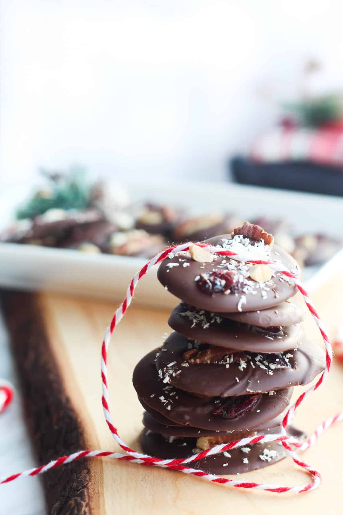 stack of round chocolate bark stacked on a piece of wood and a red and white twine placed on it. 