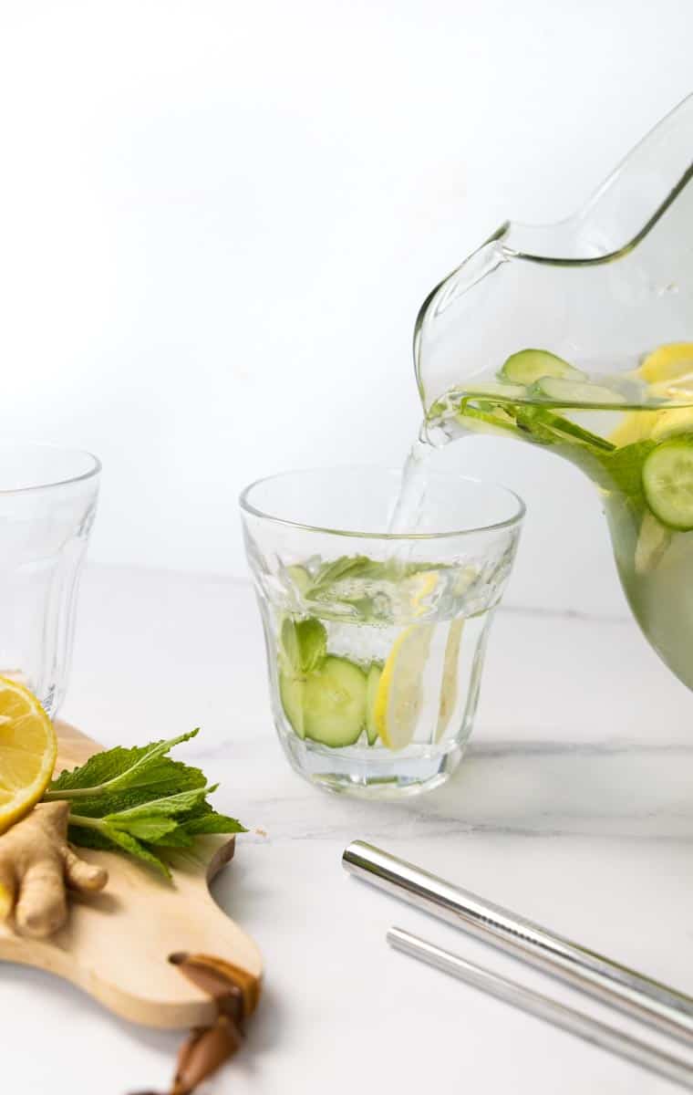 glass pitcher pouring flavoured water into a small retro looking glass.