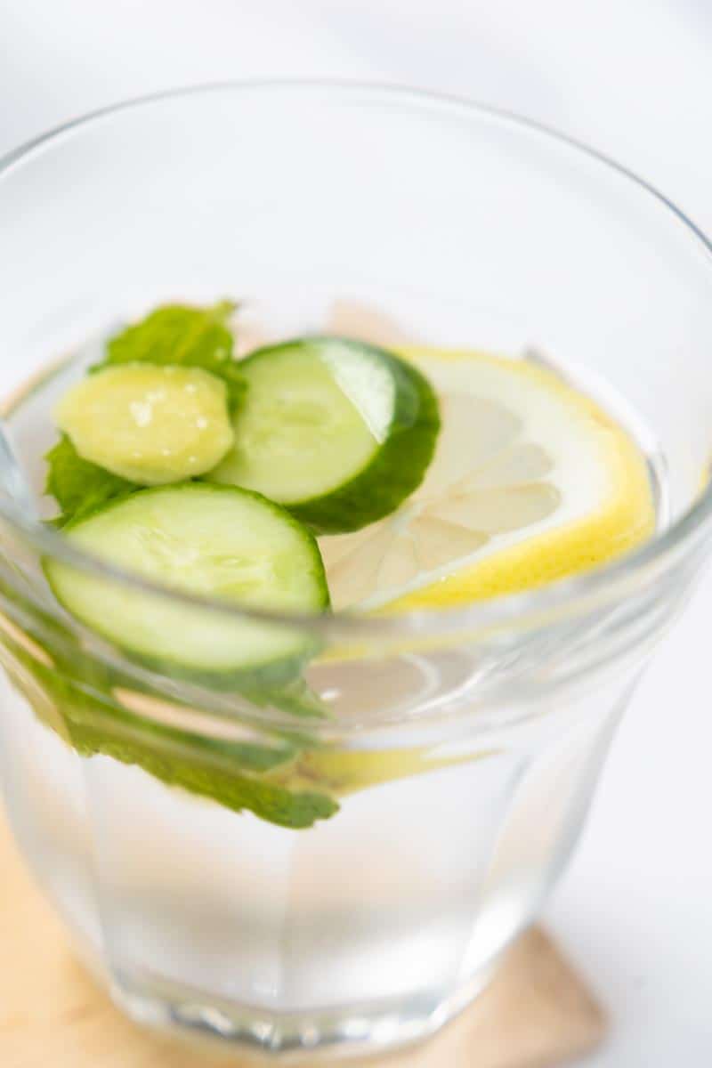 retro glass filled with water, 2 cucumber slices and a lemon slice are floating with mint leaves. 