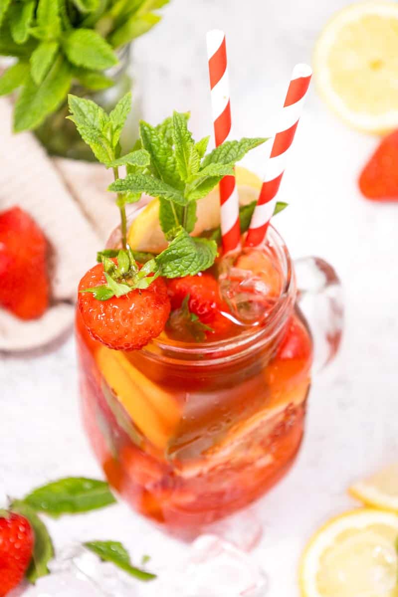 mason jar filled with a strawberry drink with a strawberry as a garnish and 2 red and white straws. 