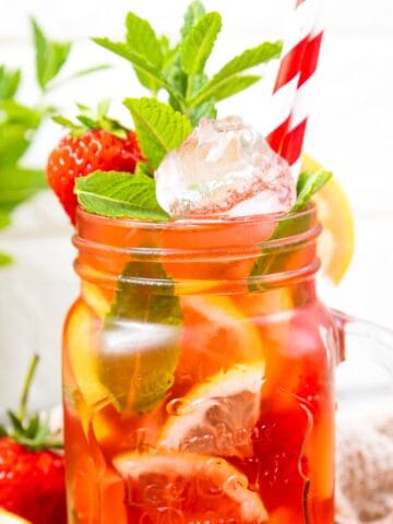 jug filled with a red juice and lemon on the side and mint leaves and 2 red and white straws.