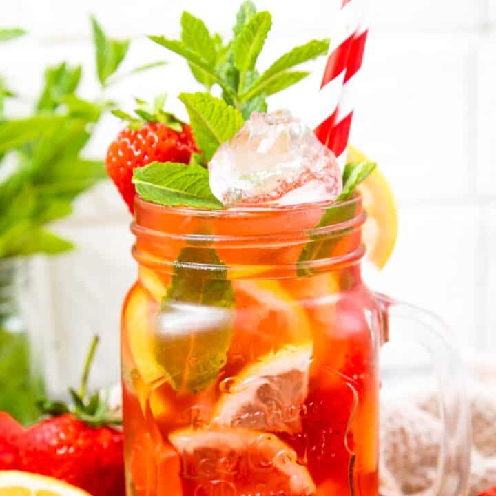 jug filled with a red juice and lemon on the side and mint leaves and 2 red and white straws.
