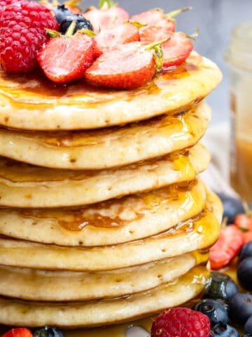Stack of 7 pancakes surrounded with berries and some on top too.
