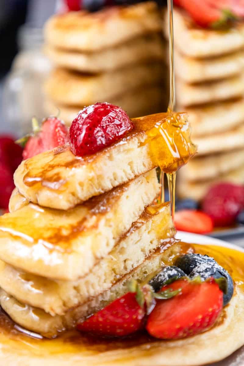 4 slices of pancakes stacked with honey dripping from the top, a few berries in the plate.