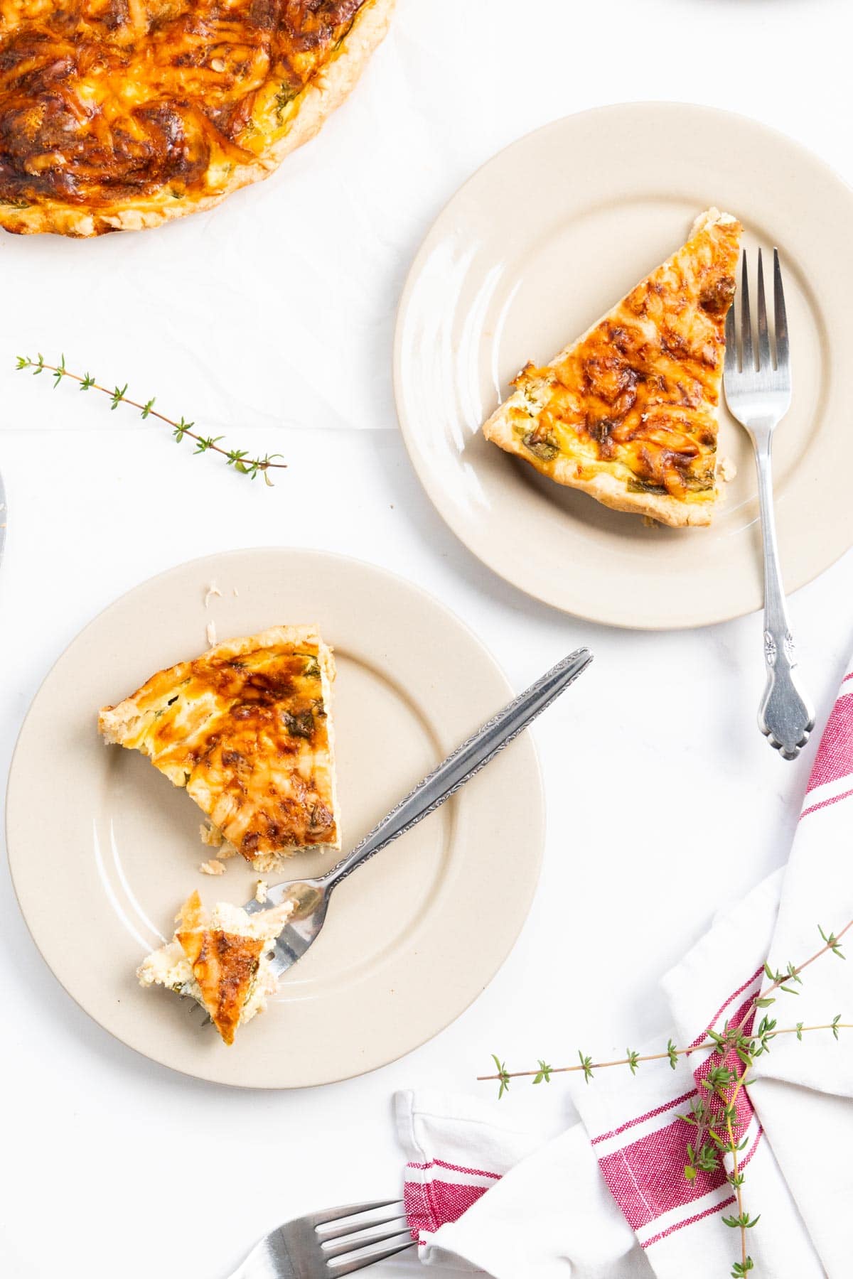 2 beige plate with a slice of quiche in it, one has a bite taken with a fork.