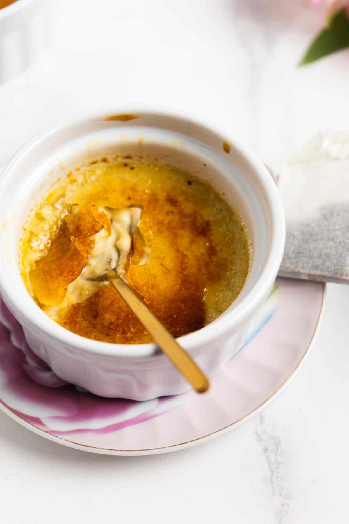 golden spoon in a white ramekin with the caramel of a creme brulee cracked.