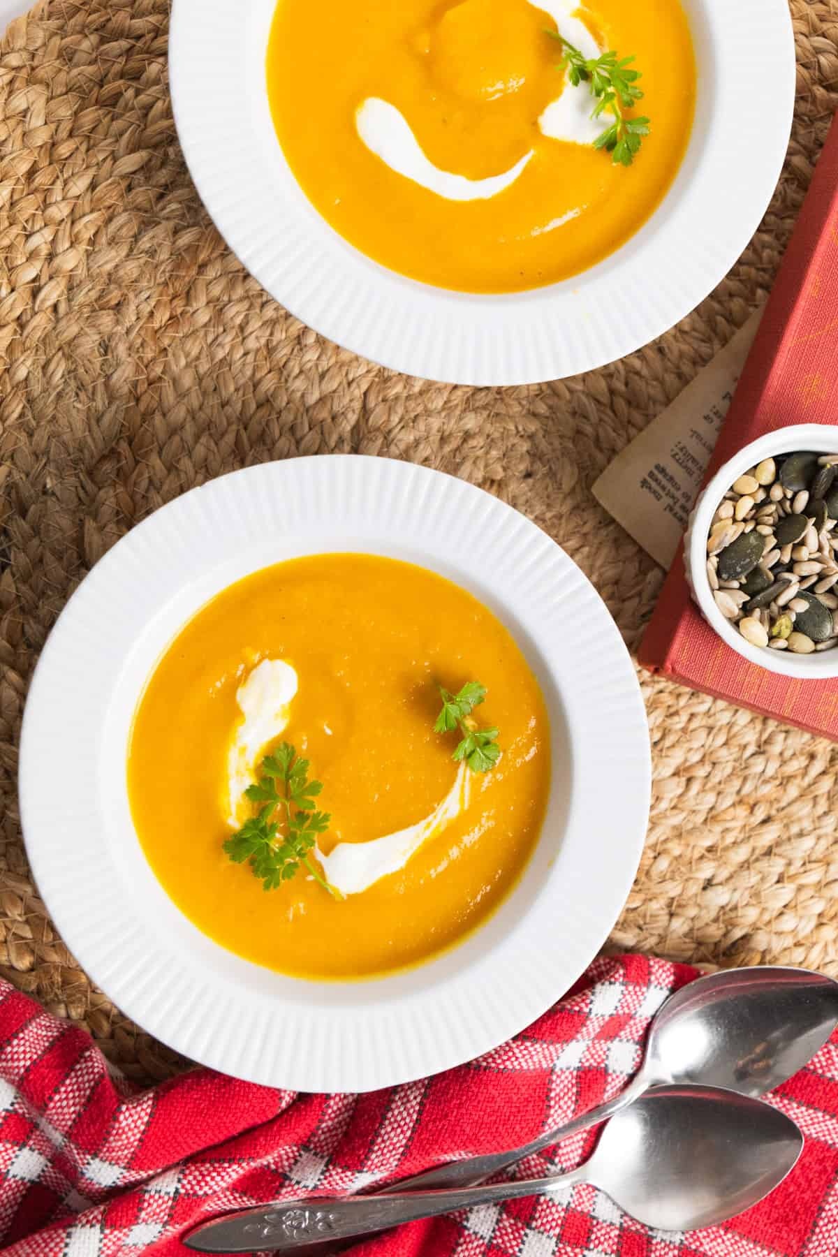 orange soup in a white bowl with a dollop of white cream and parsley as garnish. 