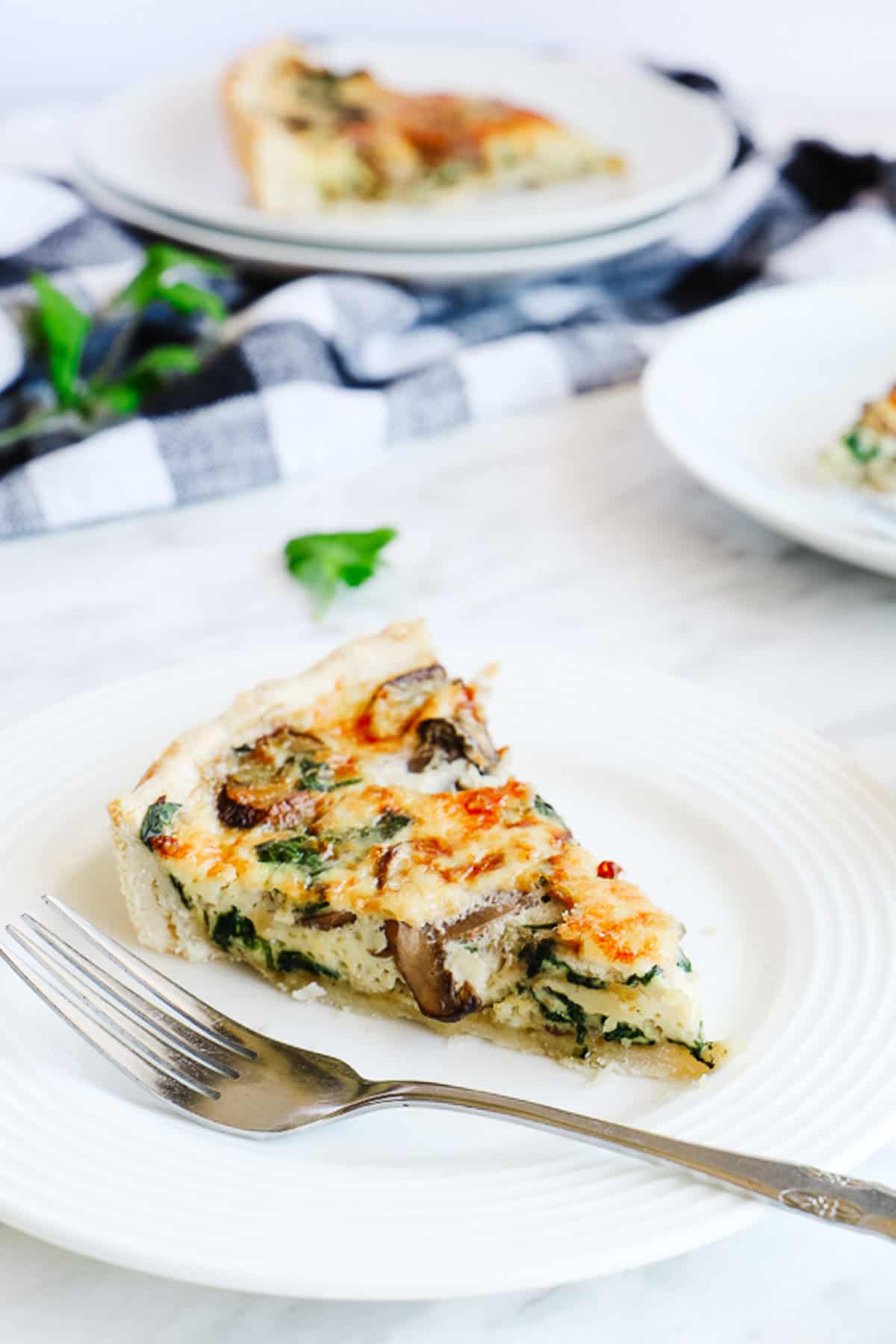 3 white plates with a slice of spinach quiche, partial view of quiche dish and cheese ramekin.