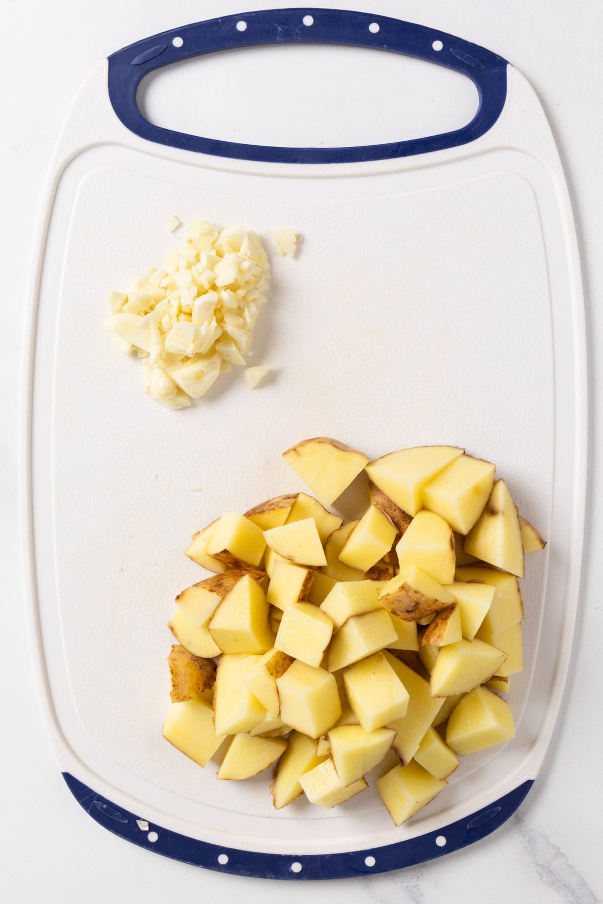 white chopping board with cubed potatoes and chopped garlic. 