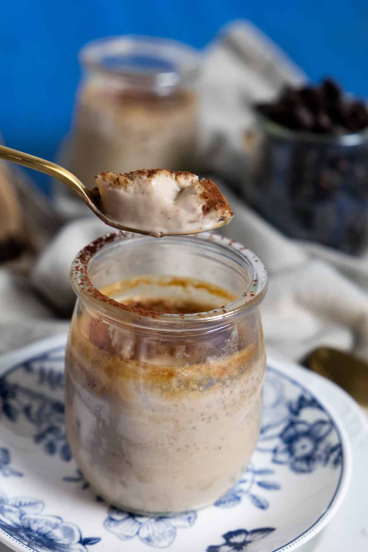 spoon holding a coffee pot de creme custard on top of a glass jar on a blue plate.