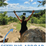 woman dressed in black raising her arms in front of a canadian lake and forest view.