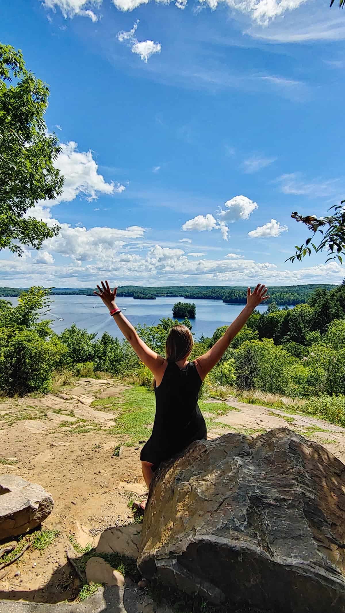 women dressed in black raising her arms in front of a canadian lake and forest. 