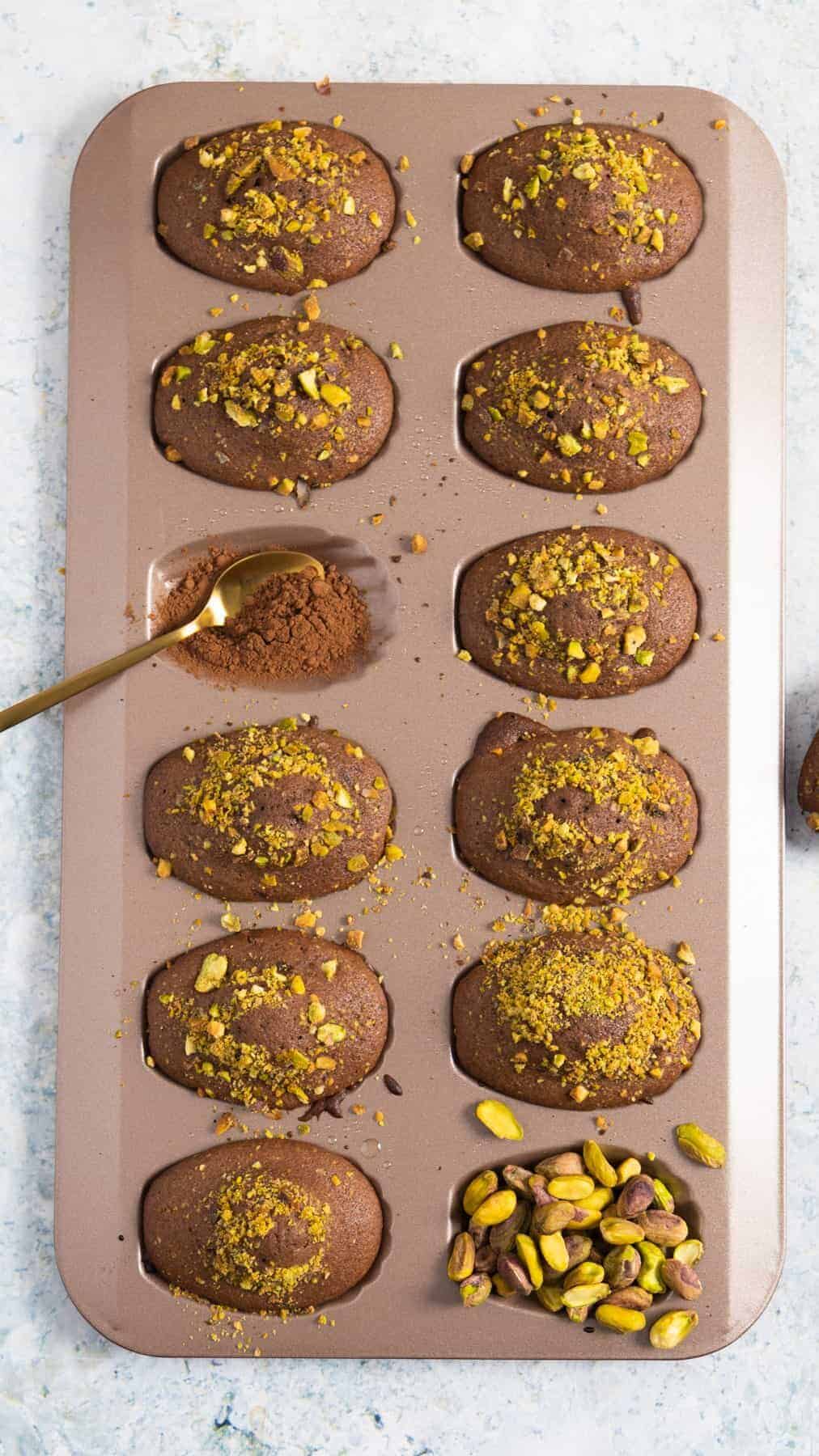 chocolate madeleines still in their mold and except one mold is filled with pistachio and one with cocoa powder.